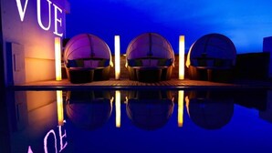 A poolside area with three sun loungers under a neon sign, a wooden deck, and a clear reflection on the water. - Hotel Paradise (Jaipur)