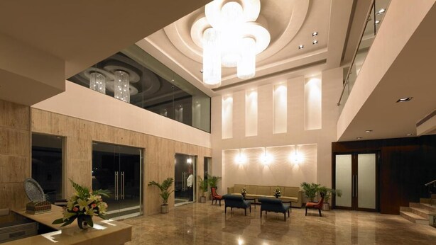 A spacious lobby with a high ceiling, a reception desk, seating area, and a staircase. - Hotel Paradise (Jaipur)