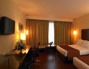 A hotel room with a bed, a desk with a chair, a TV, and a window with curtains.