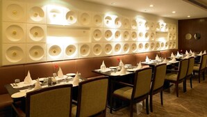 A restaurant with a long counter, multiple tables, and a decorative wall with circular patterns. - Hotel Paradise (Jaipur)