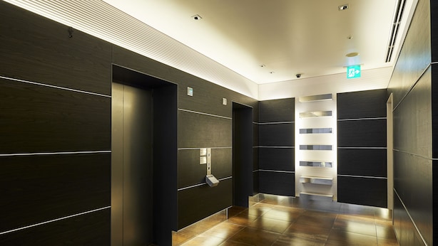 A modern elevator area with dark wood paneling and a sleek, metallic elevator door. - Sotetsu Fresa Inn Higashi Shinjuku (Tokyo)
