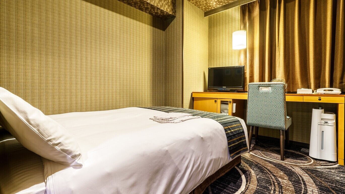 Ein Hotelzimmer mit einem Bett, einem Schreibtisch mit Computer, einem Sessel und einem Telefon.