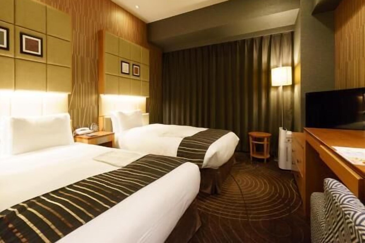 A hotel room with two beds, a desk, a television, and a small table.