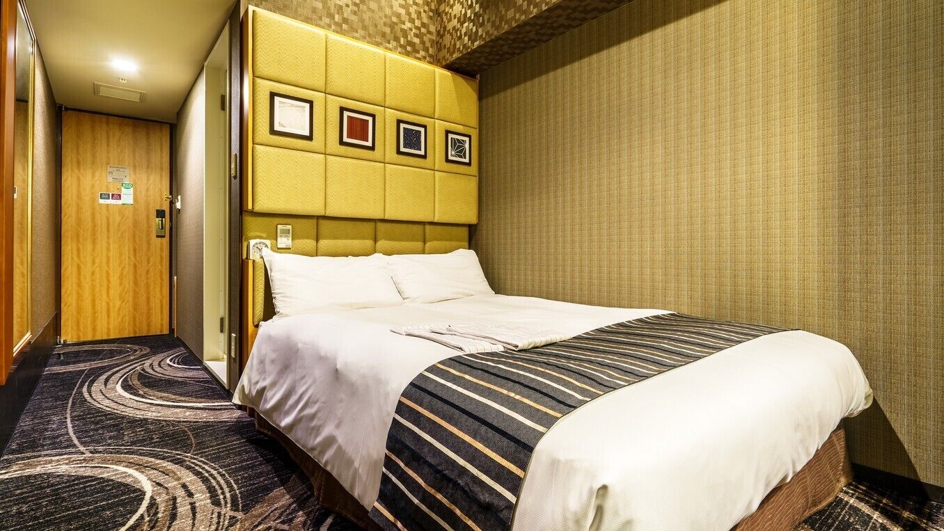 Ein Hotelzimmer mit einem großen Bett, einem Kopfteil mit gerahmten Bildern, einem Teppichboden und einer Holztür.