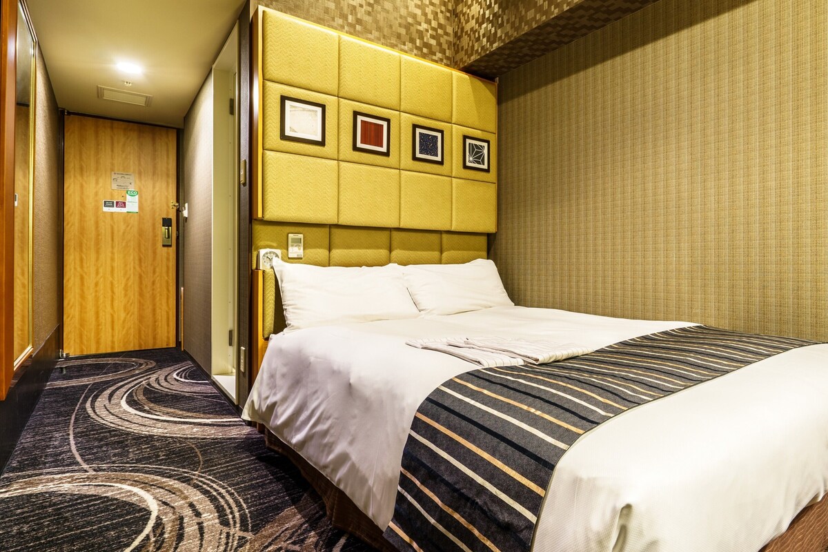 A hotel room with a bed, a headboard with framed pictures, a carpeted floor, and a door with an 'eco' sign.