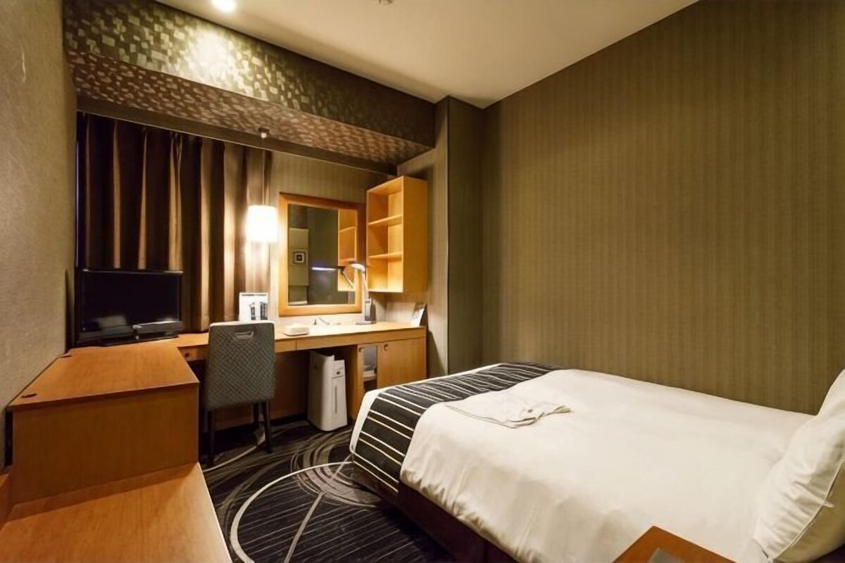 A hotel room with a bed, desk, chair, and a television.