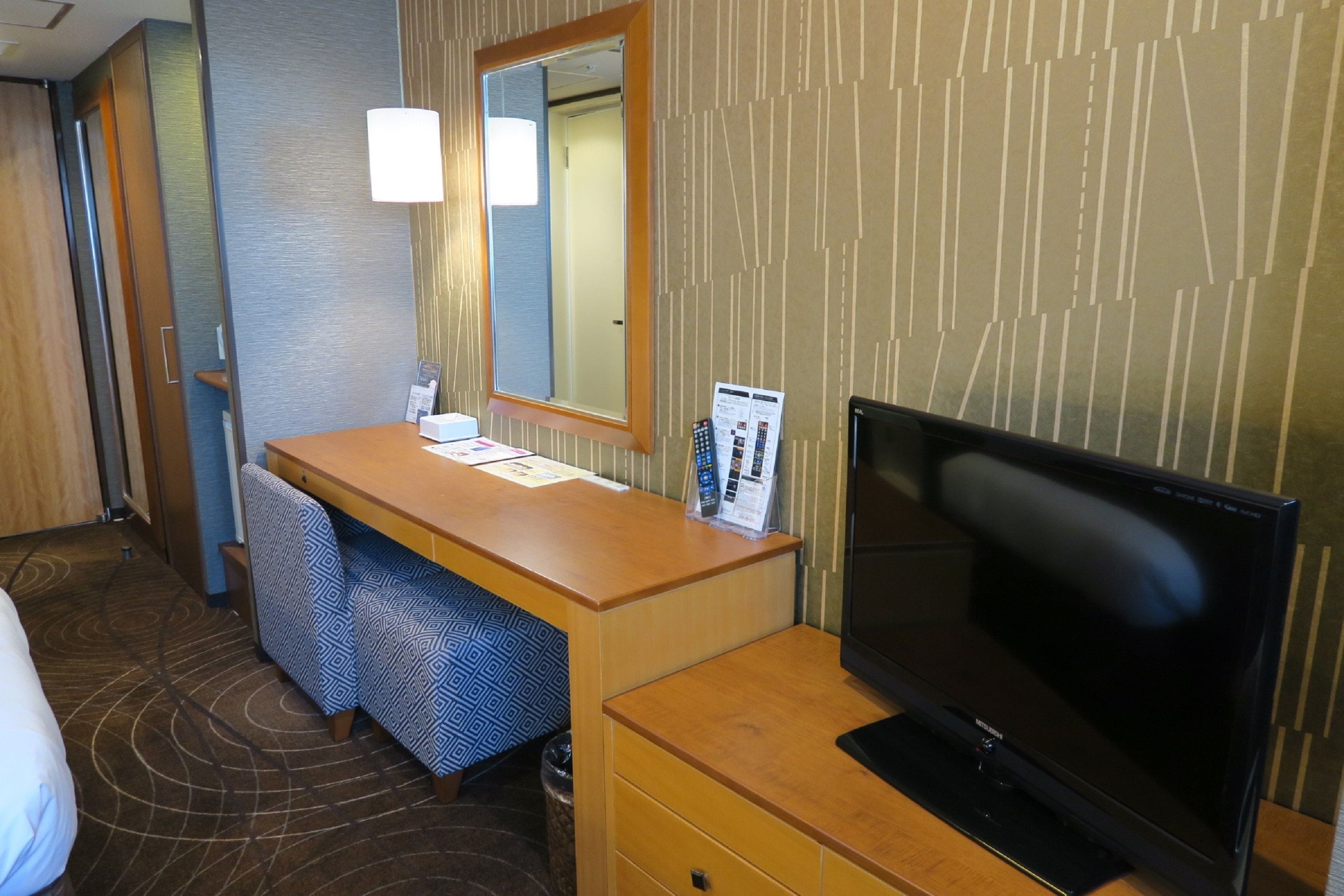 Habitación de hotel con escritorio de madera, televisor, espejo y pared con diseño.