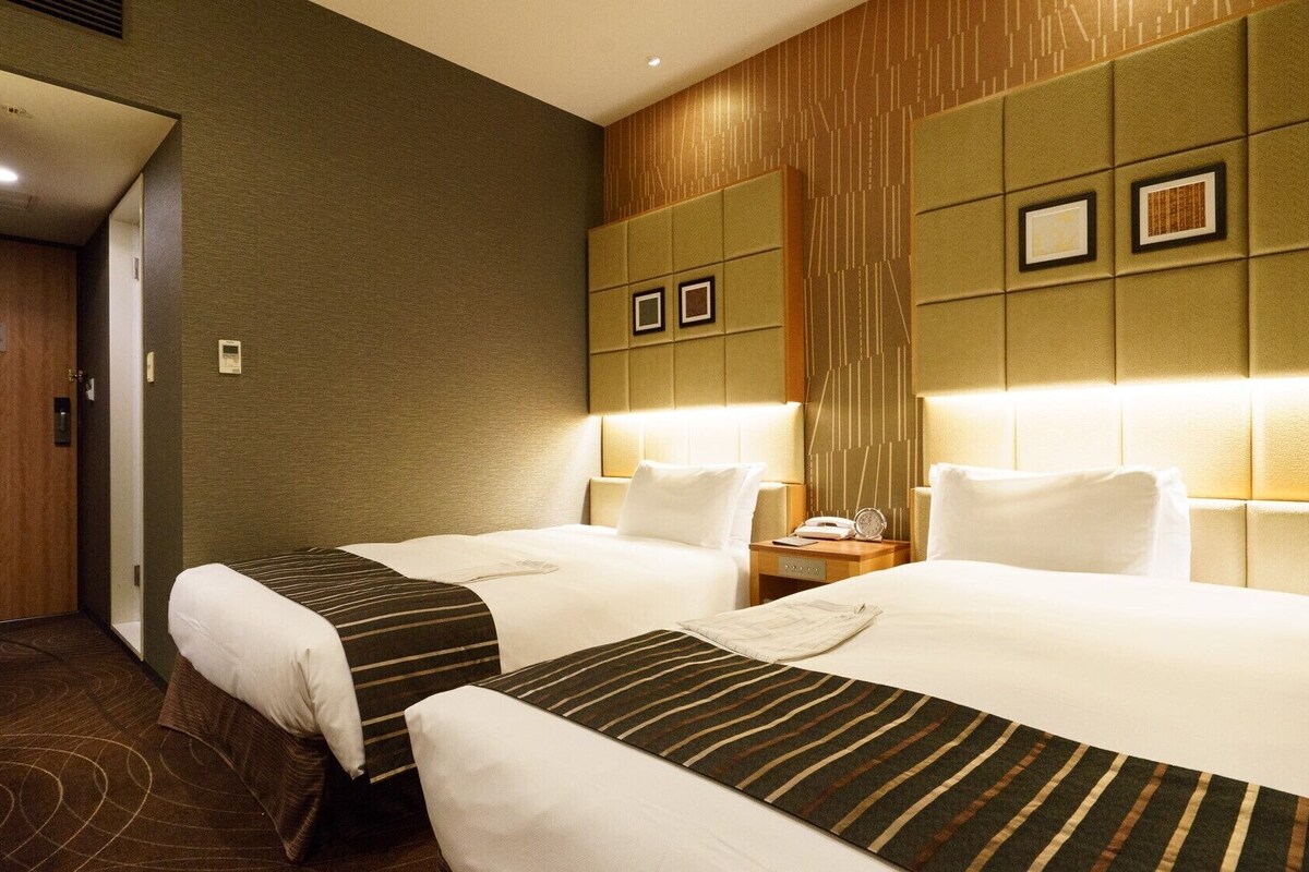 A hotel room with two beds, a wooden door, and a wall with framed pictures.