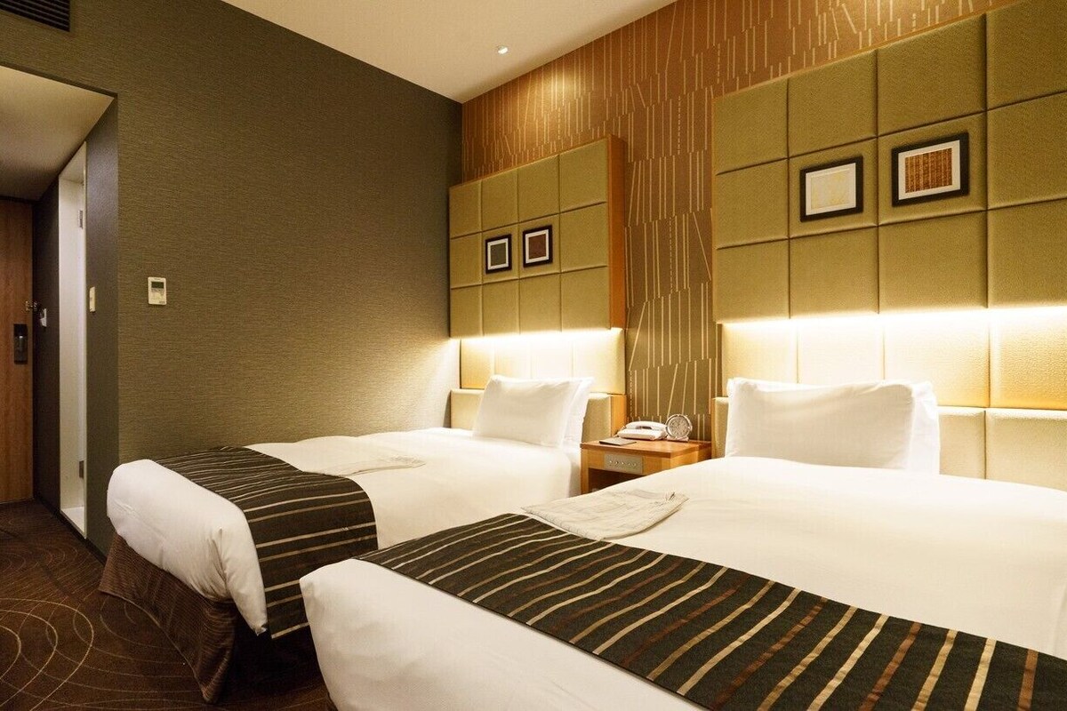 A hotel room with two beds, a wooden door, and a wall with framed pictures.