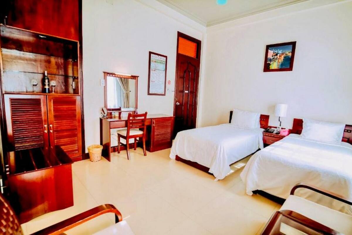 A hotel room with two beds, a desk, a chair, a wardrobe, and a mirror.
