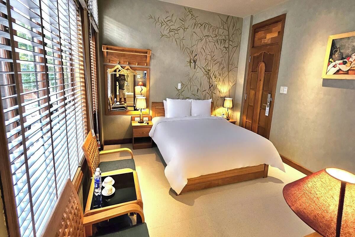 A hotel room with a large bed, a desk, a chair, a wardrobe, and a ceiling fan.