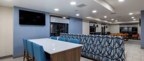 A modern dining area with a long table and blue chairs, a patterned partition, and a flat-screen TV on the wall.