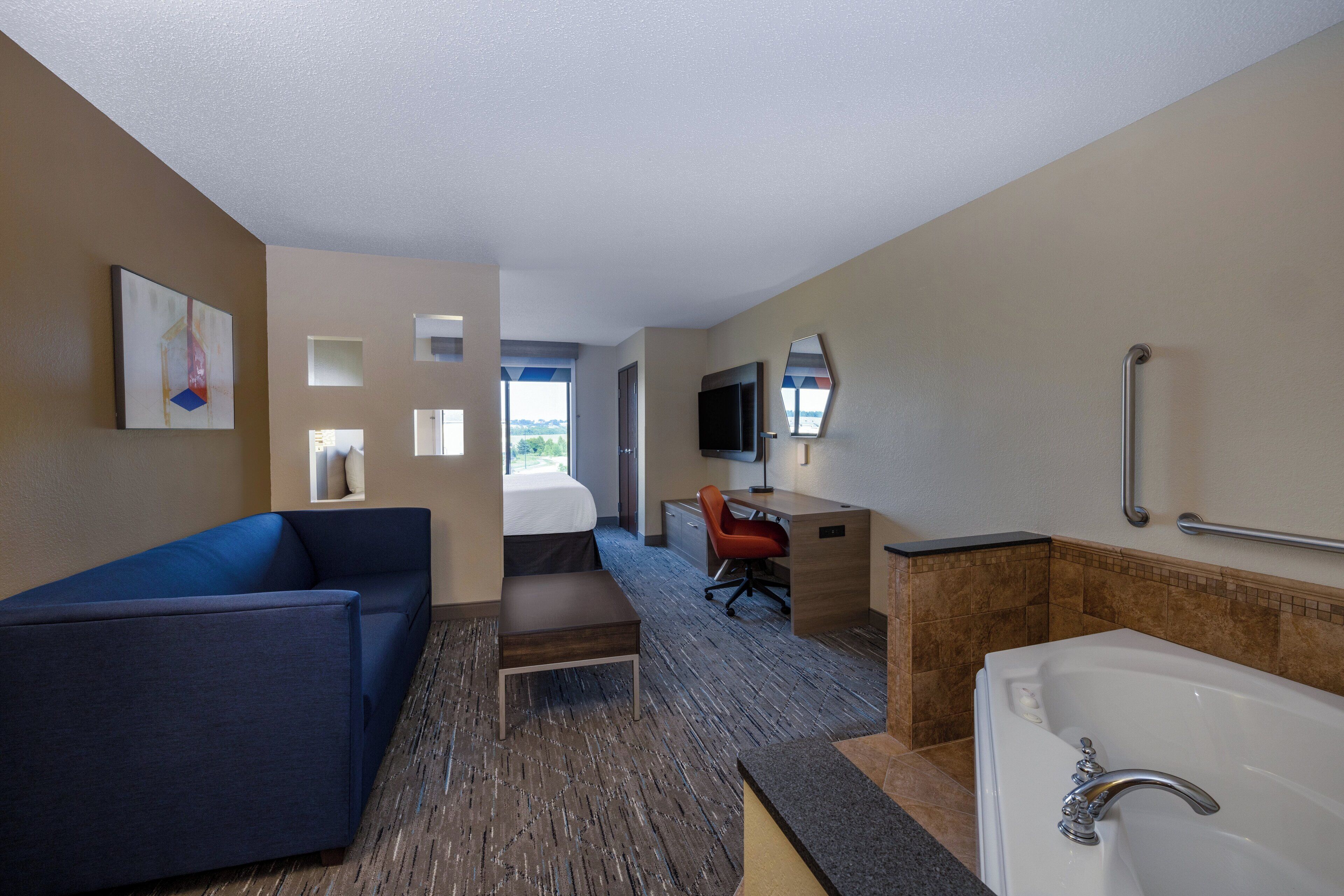 A hotel room with a bed, a desk, a chair, a sofa, a bathtub, and a television.