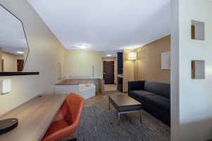 Una habitación de hotel moderna con un escritorio de madera, una silla naranja, un sofá oscuro y una mesita.