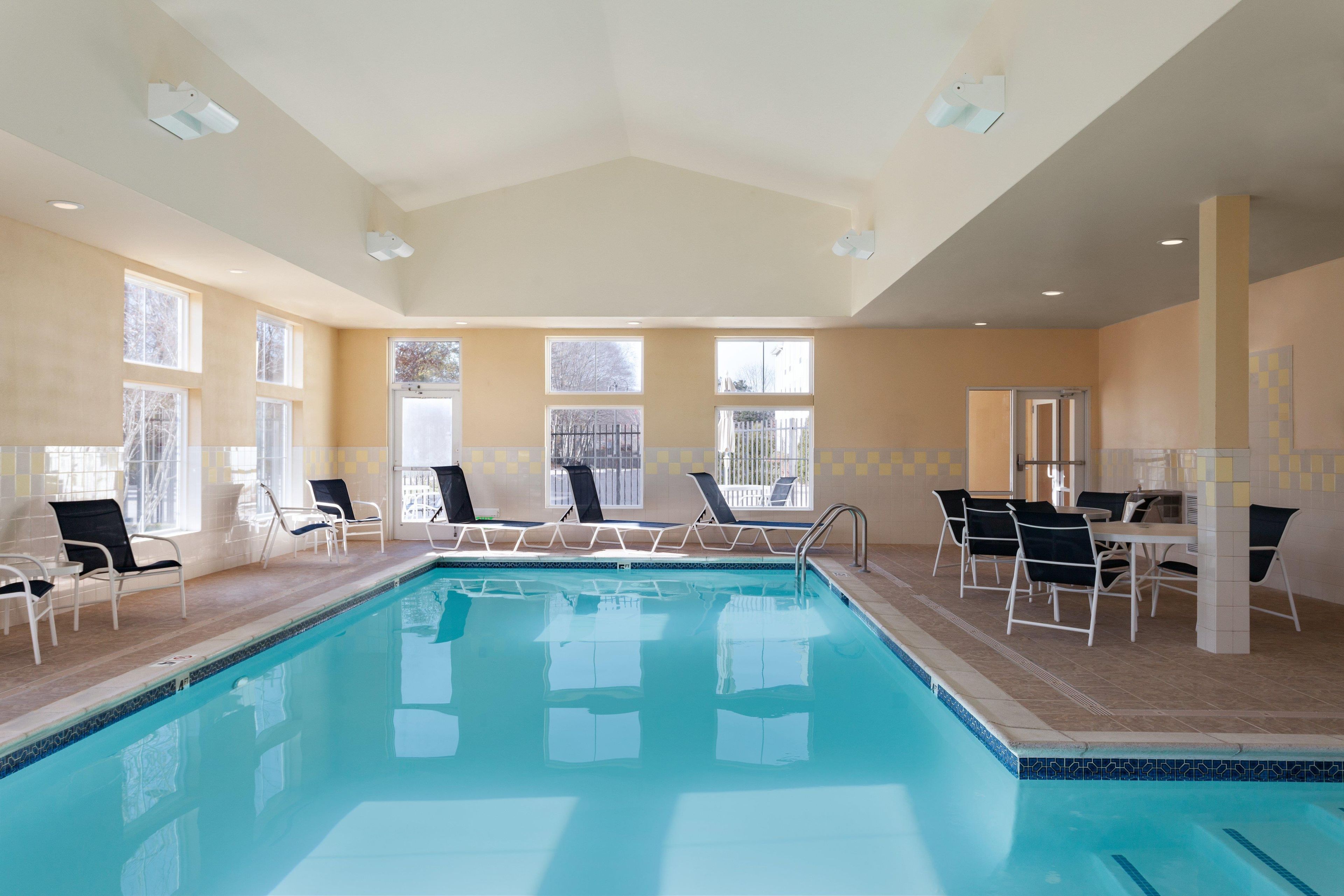 Ein Swimmingpool mit Liegestühlen und einem Tisch, umgeben von Fenstern.