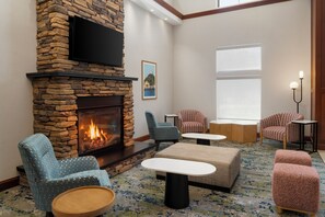 A room with a stone fireplace, comfortable seating, a flat-screen TV, and a large window.