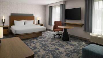 Habitación de hotel con cama, escritorio, silla, televisor y ventana con cortinas.