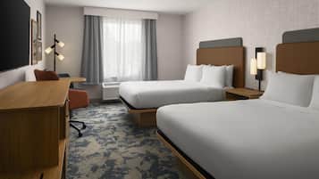Habitación de hotel con dos camas, un escritorio, una silla, un ventanal con cortinas y una lámpara de pared.