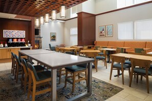 A restaurant with a long communal table, individual booths, and a bar area with coffee dispensers.
