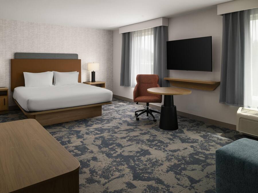 A hotel room with a bed, a desk, a chair, a TV, and a window with curtains.