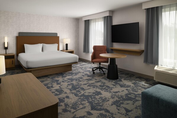 A hotel room with a bed, a desk, a chair, a TV, and a window with curtains.