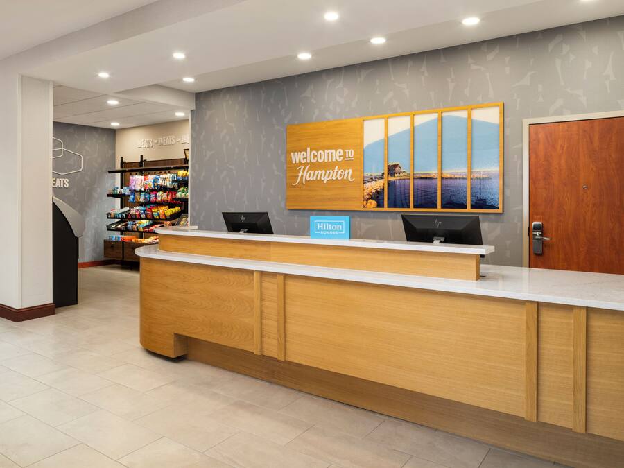 A hotel reception desk with a 'Welcome to Hampton' sign, a computer, and a snack display.
