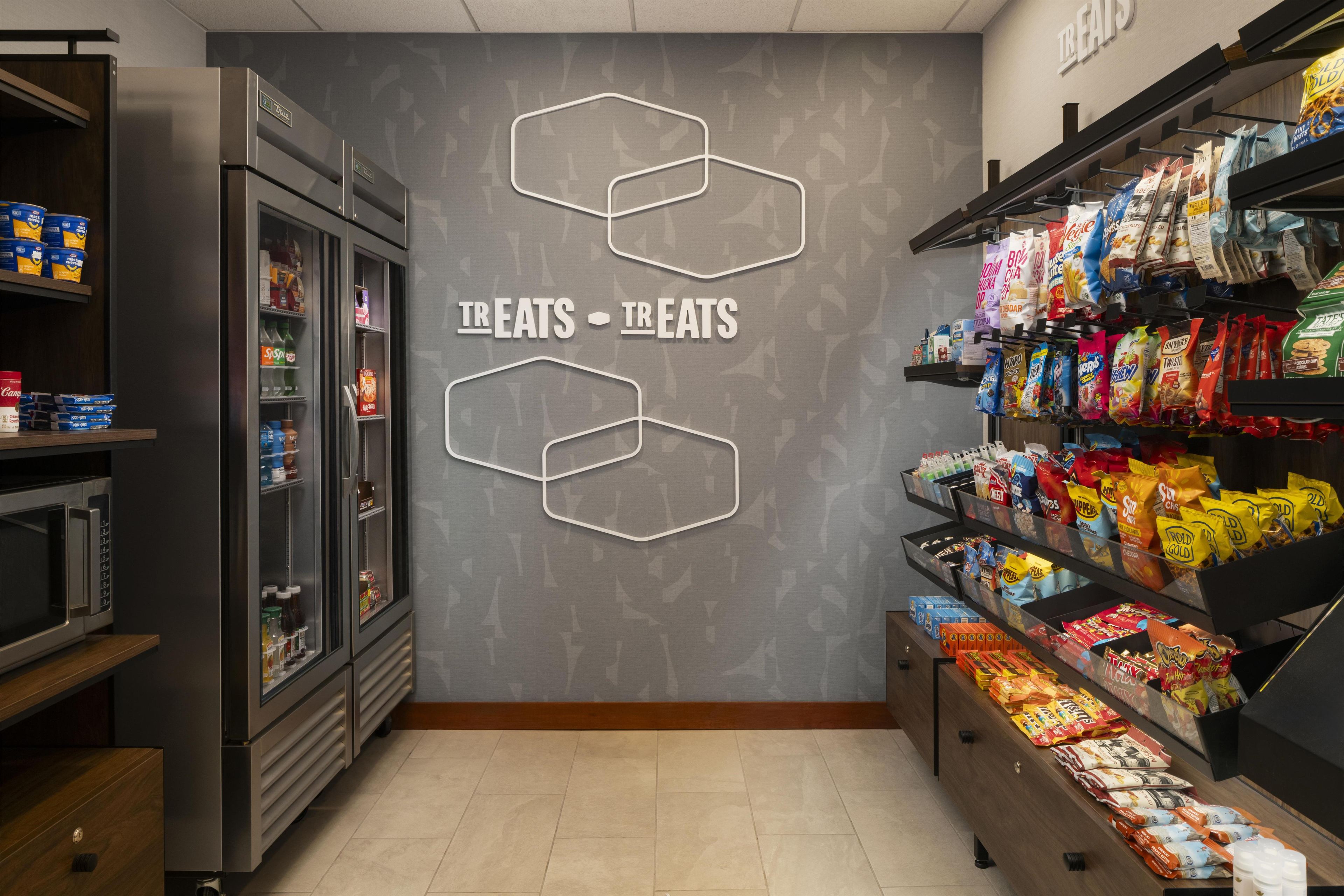 Interior de un supermercado con secciones refrigeradas, pasillos de bocadillos y una pared con patrones hexagonales.
