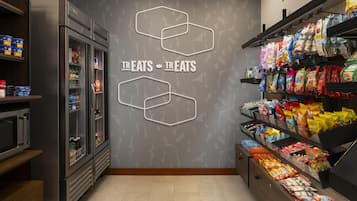 Interior de un supermercado con secciones refrigeradas, pasillos de bocadillos y una pared con patrones hexagonales.