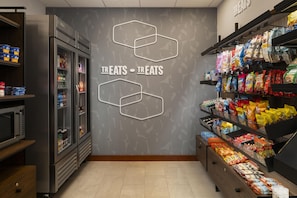 A grocery store interior with refrigerated sections, snack aisles, and a wall with hexagonal patterns.