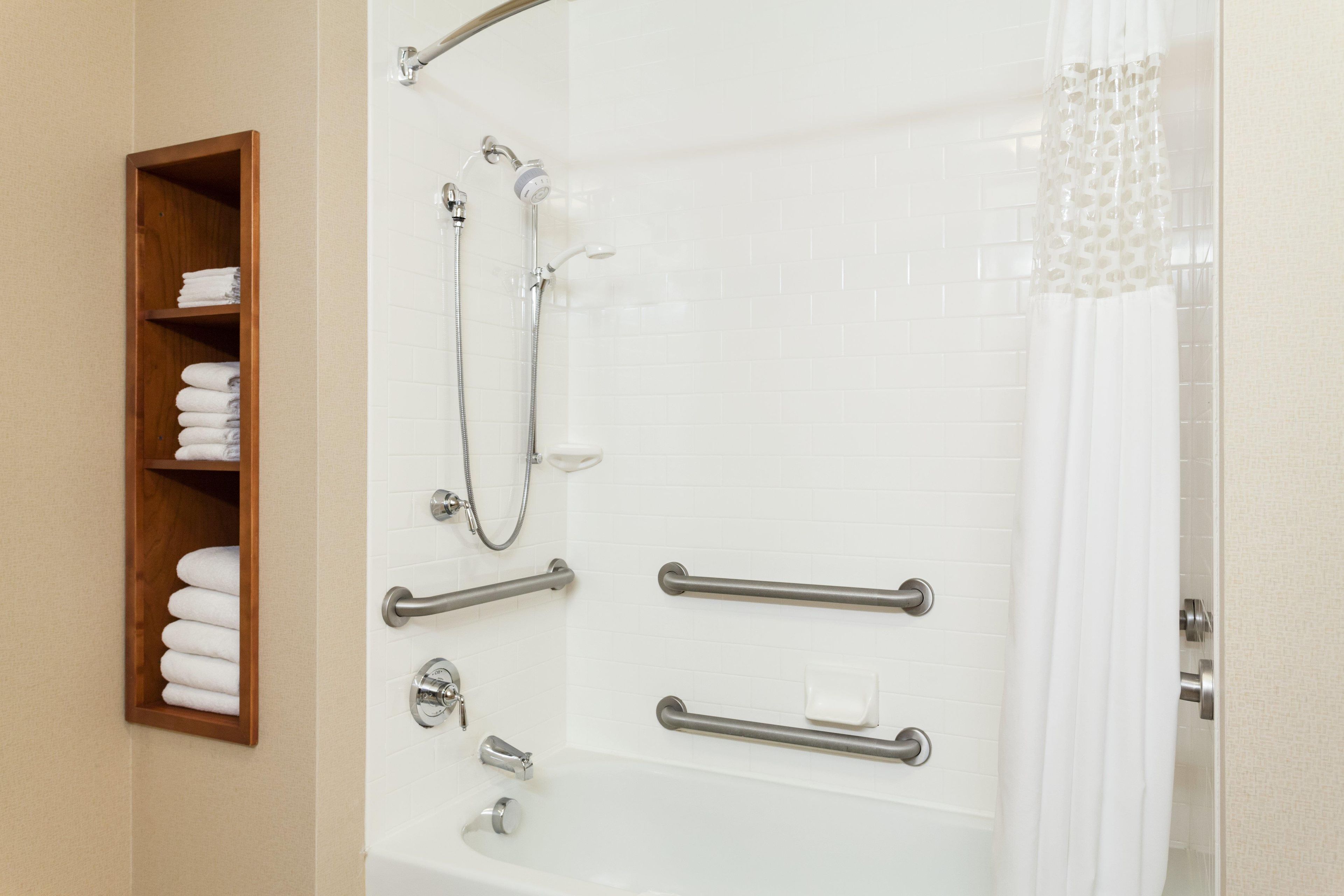 Ein Badezimmer mit barrierefreier Dusche, Haltegriffen, einem Handtuchhalter und einer Duschvorhang.