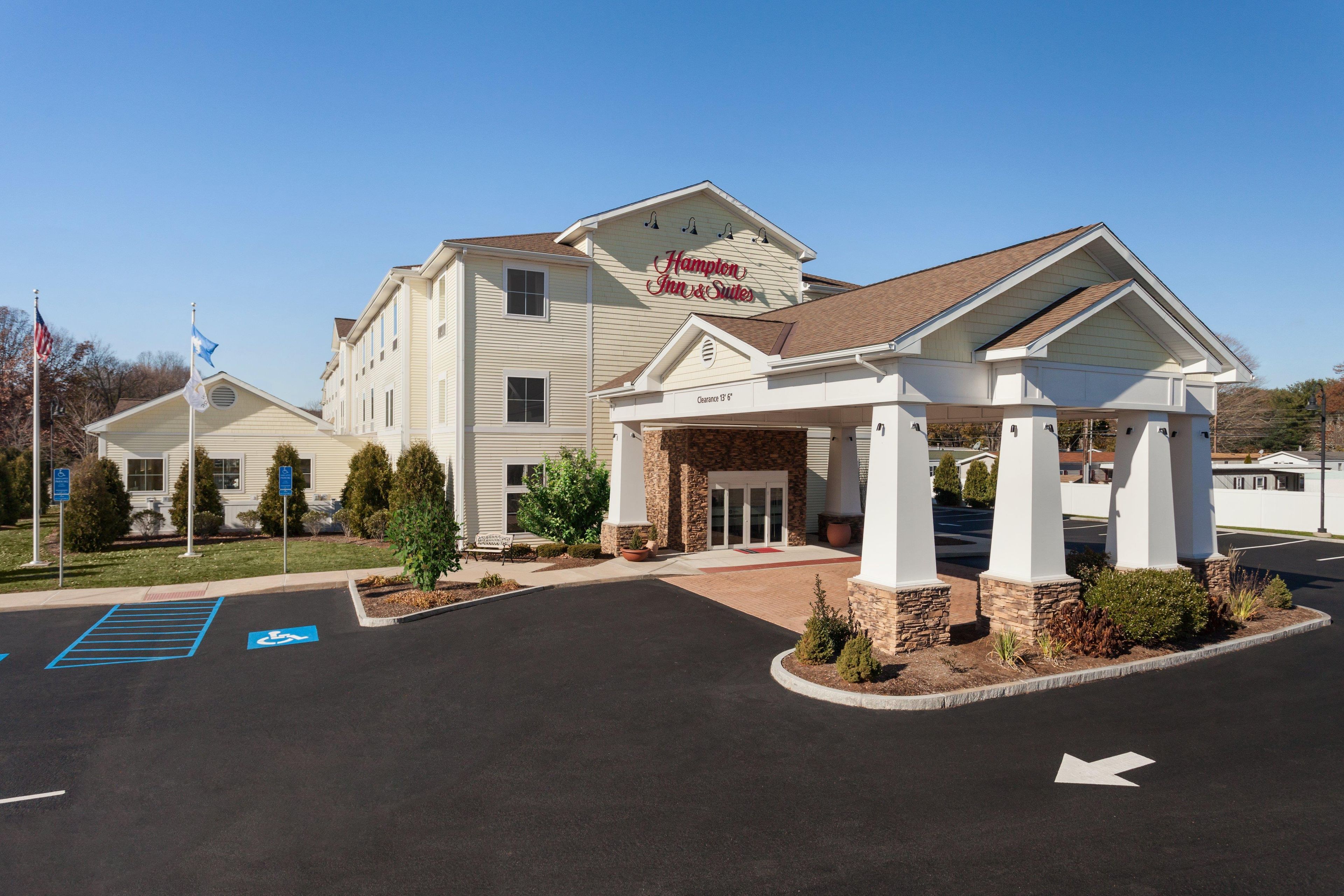 Ein Hampton Inn & Suites mit überdachtem Eingang, barrierefreiem Parkplatz und blauem Himmel.