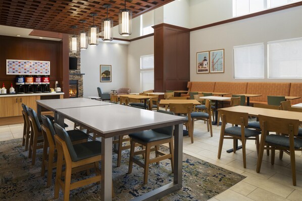 A restaurant with a long communal table, individual tables, and booths. There are coffee dispensers labeled with different types of coffee.