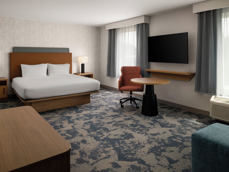 A hotel room with a bed, a desk, a chair, a TV, and a window with curtains.
