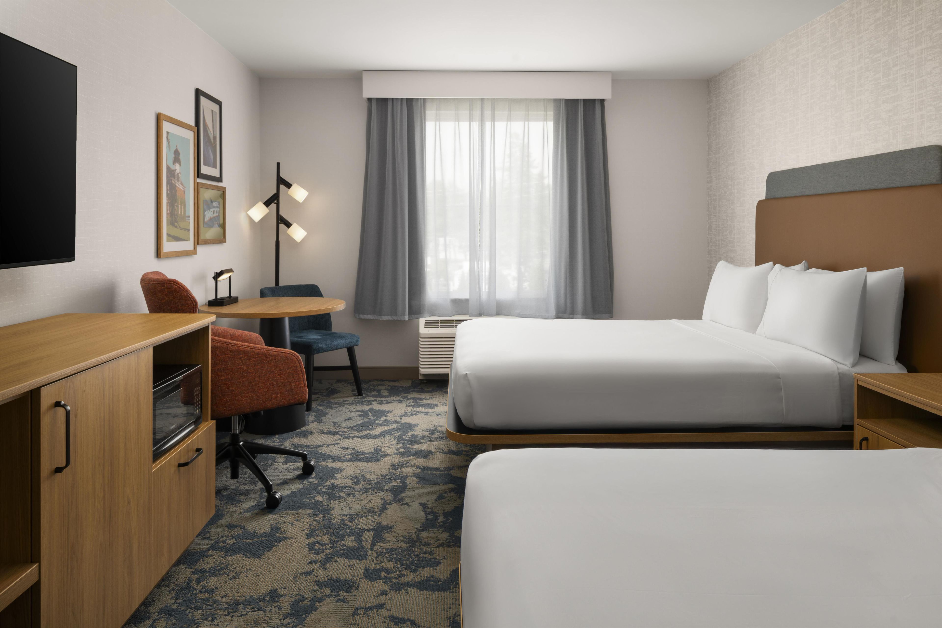 A hotel room with a bed, a desk, a chair, a TV, and a window with curtains.