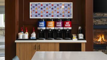 A coffee station with four dispensers labeled DARK ROAST, LIGHT ROAST, DECAF ROAST, and HOT WATER, and a wall-mounted coffee cup display above.