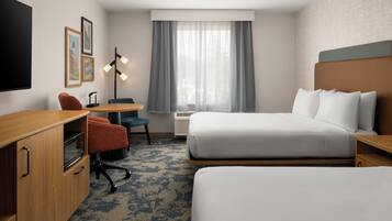 Quarto de hotel com cama, escrivaninha, cadeira, televisão e janela com cortinas.