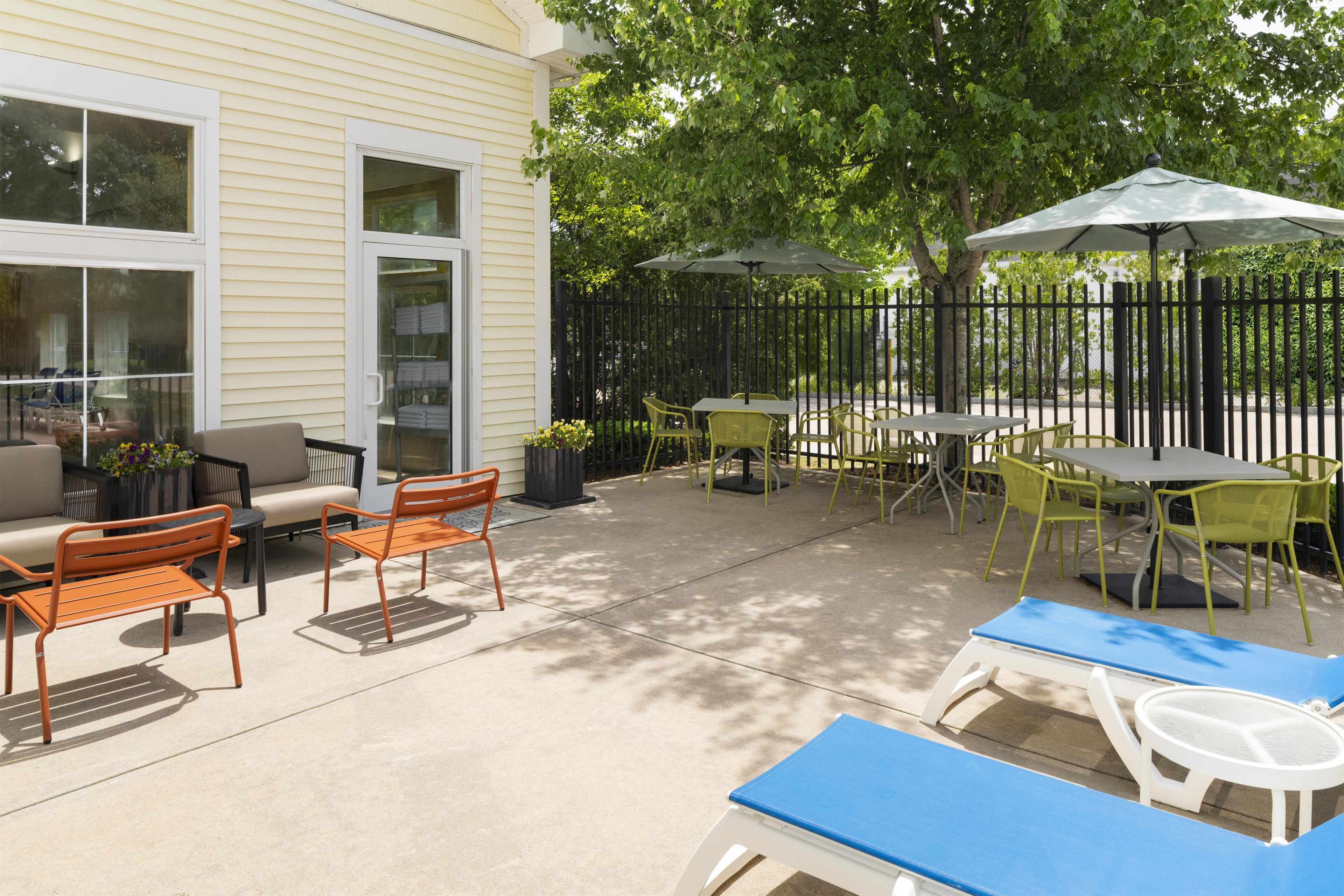 An outdoor patio area with seating arrangements, including chairs and tables, and a covered section with umbrellas.