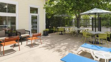 An outdoor patio area with seating arrangements, including chairs and tables, and a covered section with umbrellas.
