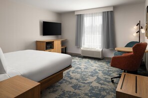 A hotel room with a bed, a desk, a chair, a television, an air conditioning unit, and a window with curtains.
