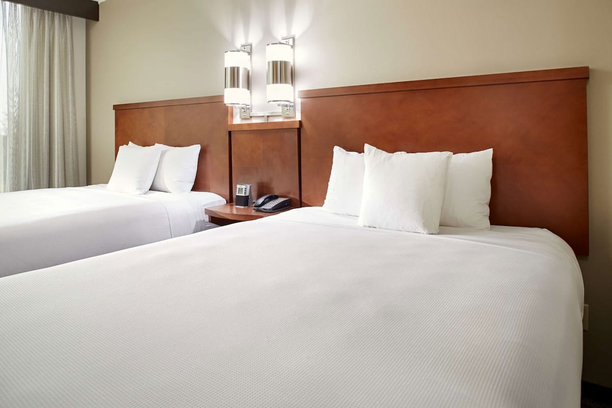 Une chambre d’hôtel avec deux lits, une table de chevet avec un téléphone et des lampes fixées au mur.