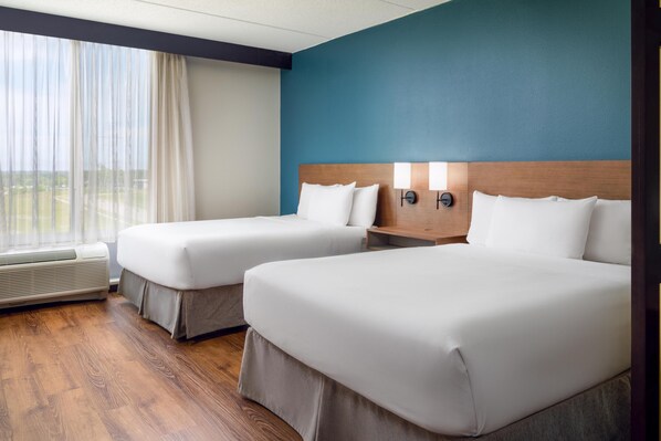 A hotel room with two beds, a wooden headboard, a nightstand with lamps, and a large window with curtains. - Hyatt Place Grand Rapids-South (Wyoming)