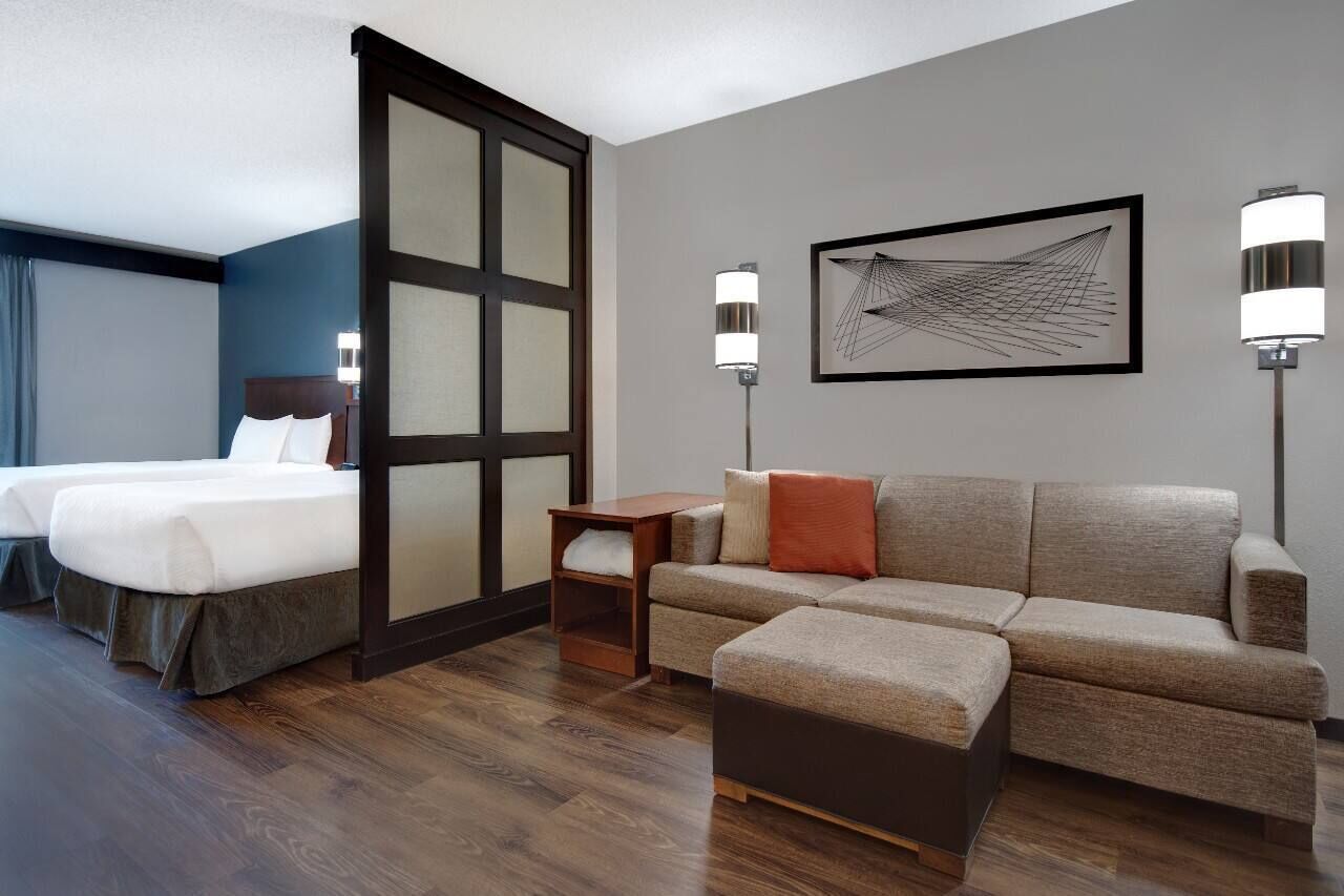 Una habitación de hotel con una cama, un sofá, una mesita y una obra de arte colgada en la pared.