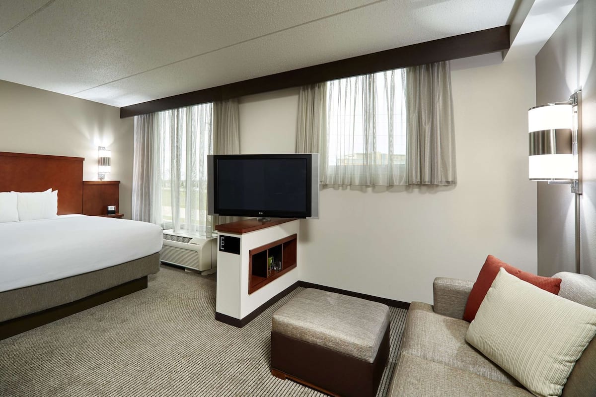 Une chambre d’hôtel avec un grand lit, un téléviseur à écran plat, un canapé et une petite table avec une lampe.
