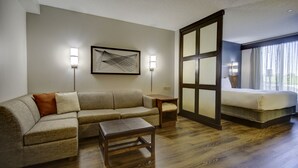 Ein Hotelzimmer mit einer Couch, einem kleinen Tisch, einem Bett und einem großen Fenster mit Vorhängen.