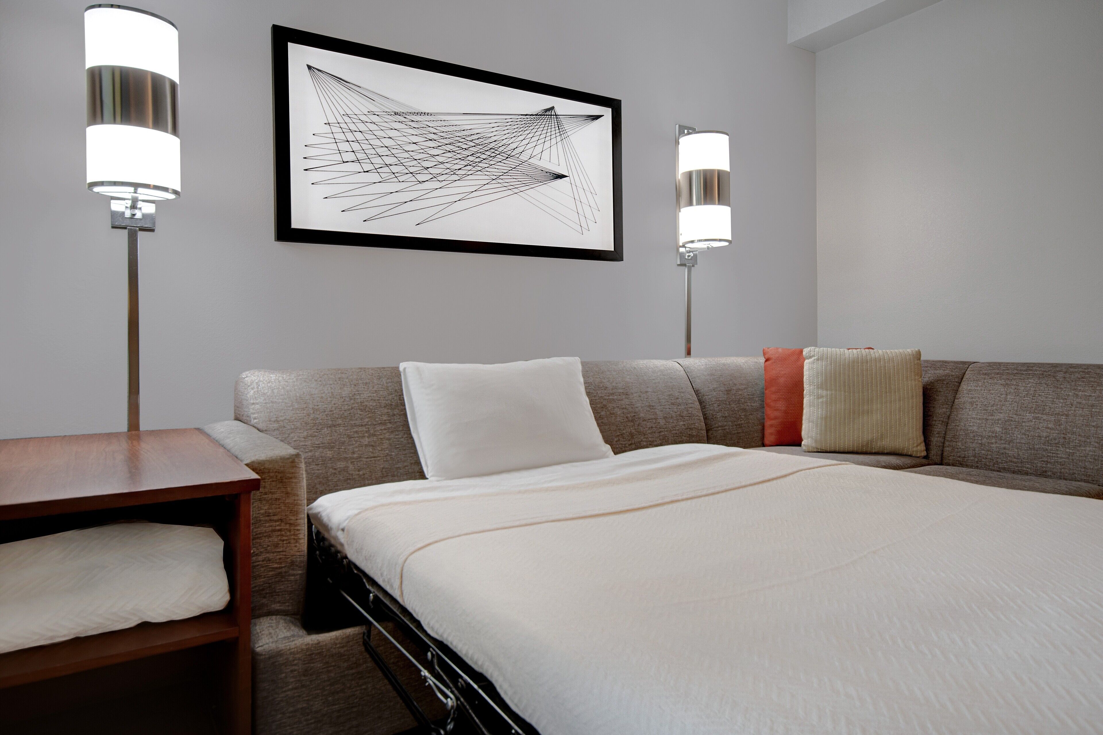 A hotel room with a bed, a bedside table, a chair, and two wall-mounted lamps.