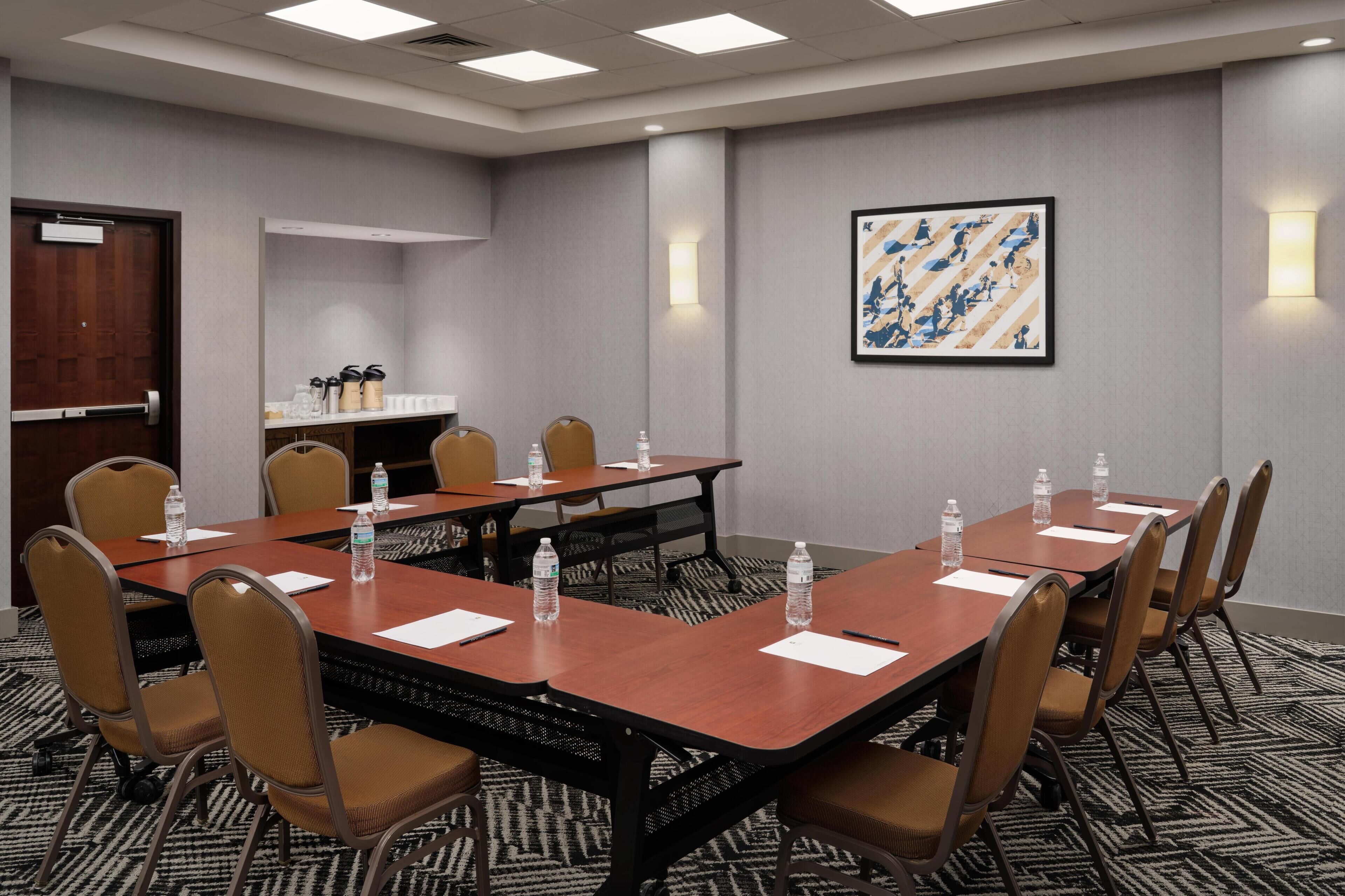 Uma sala de conferências com uma mesa comprida, cadeiras, garrafas de água e uma pintura abstrata emoldurada na parede.