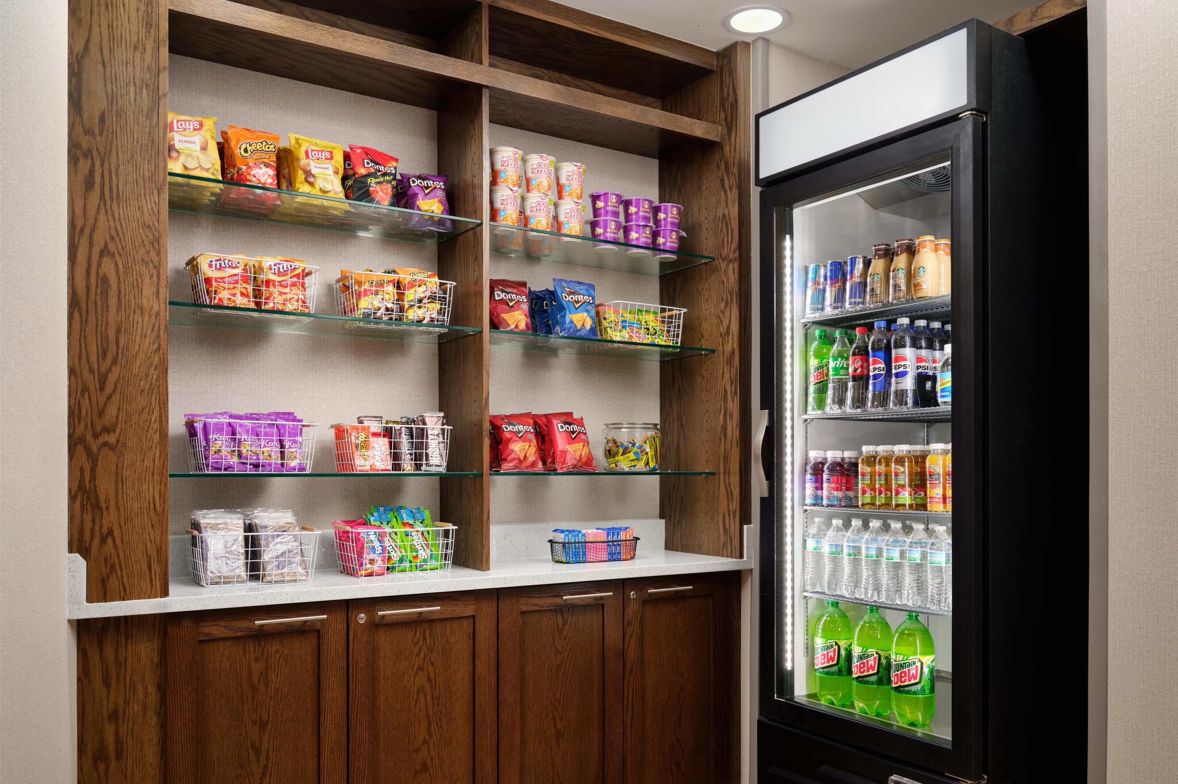A kitchenette with shelves stocked with snacks, a refrigerator with beverages, and a microwave.