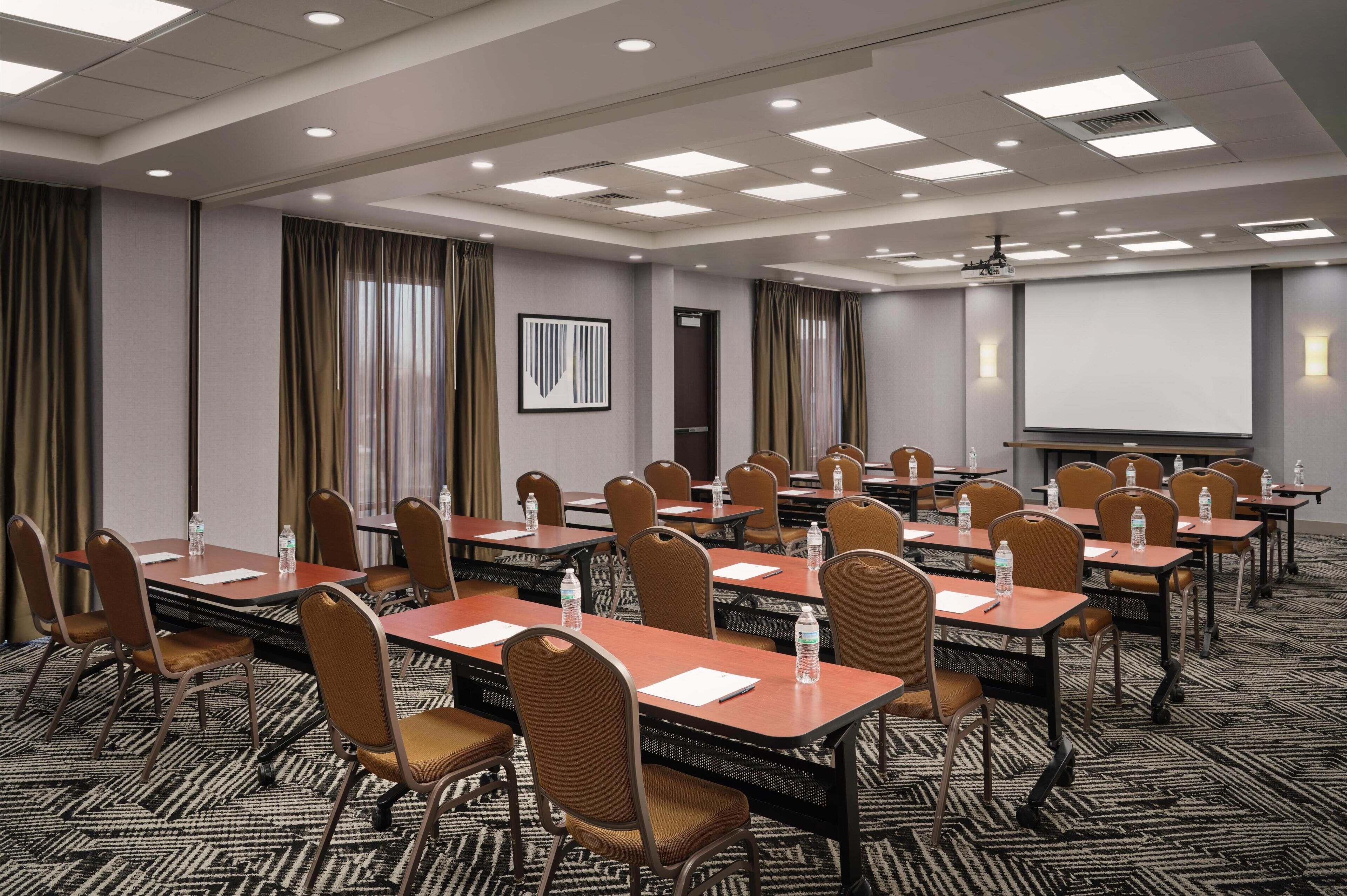 A conference room with multiple tables, chairs, a projector screen, and a carpeted floor.