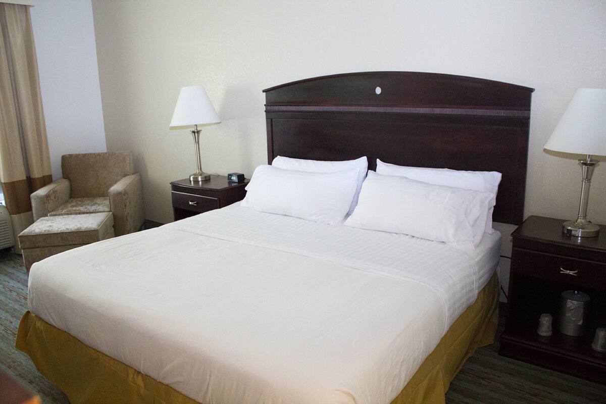 A hotel room with a large bed, two bedside tables, a chair, and a lamp.
