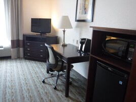 Habitación de hotel con escritorio, una silla, televisor, lámpara, cafetera, microondas y refrigerador.